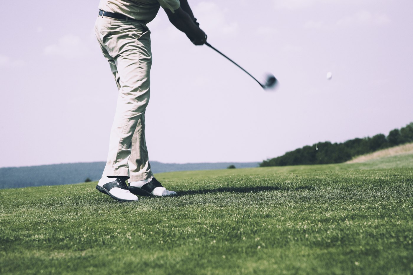 Golfista batendo com um driver no tee, visto de baixo, com a bola já no ar sobre o fairway.